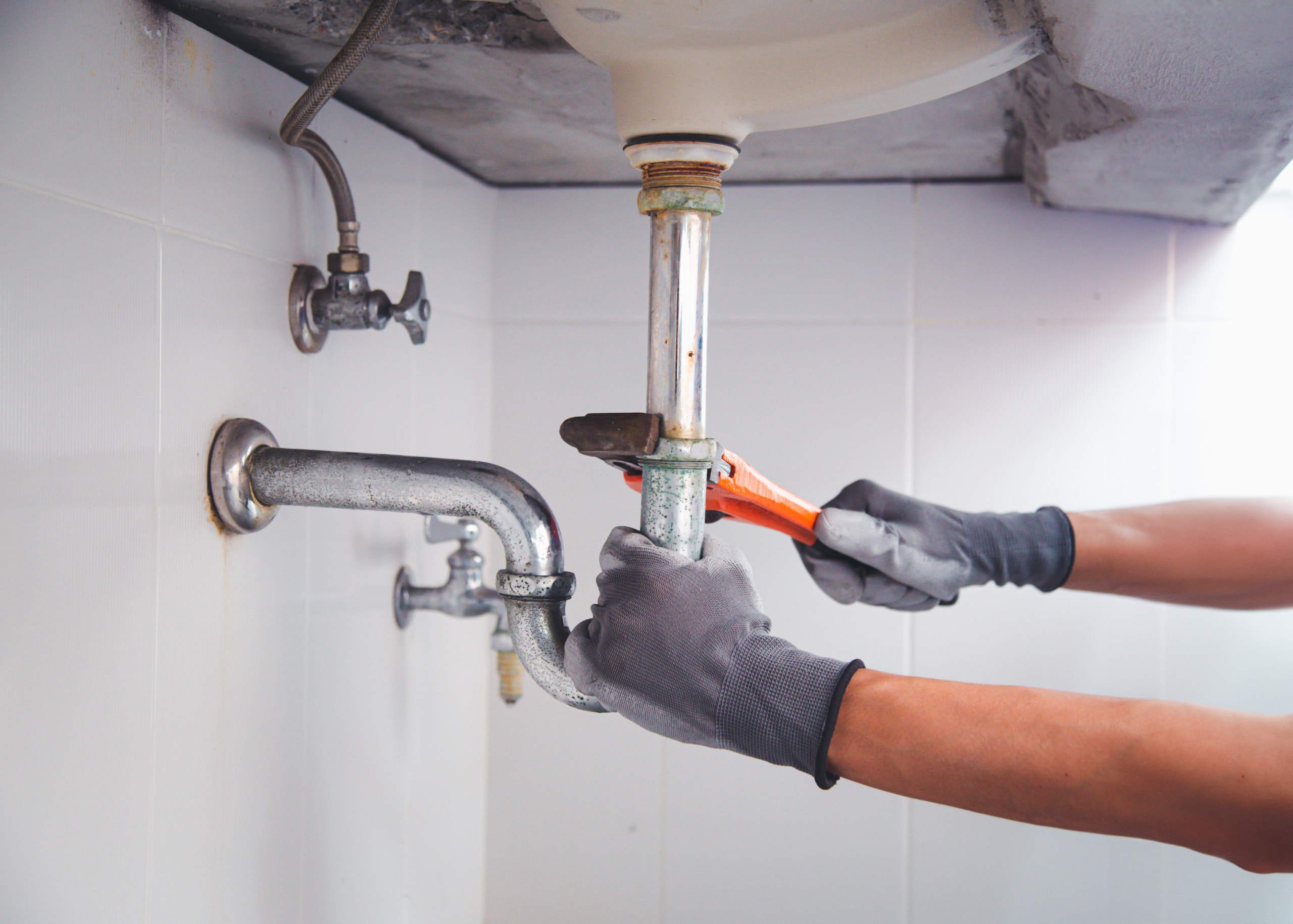 Technician plumber using a wrench to repair a water pipe under t