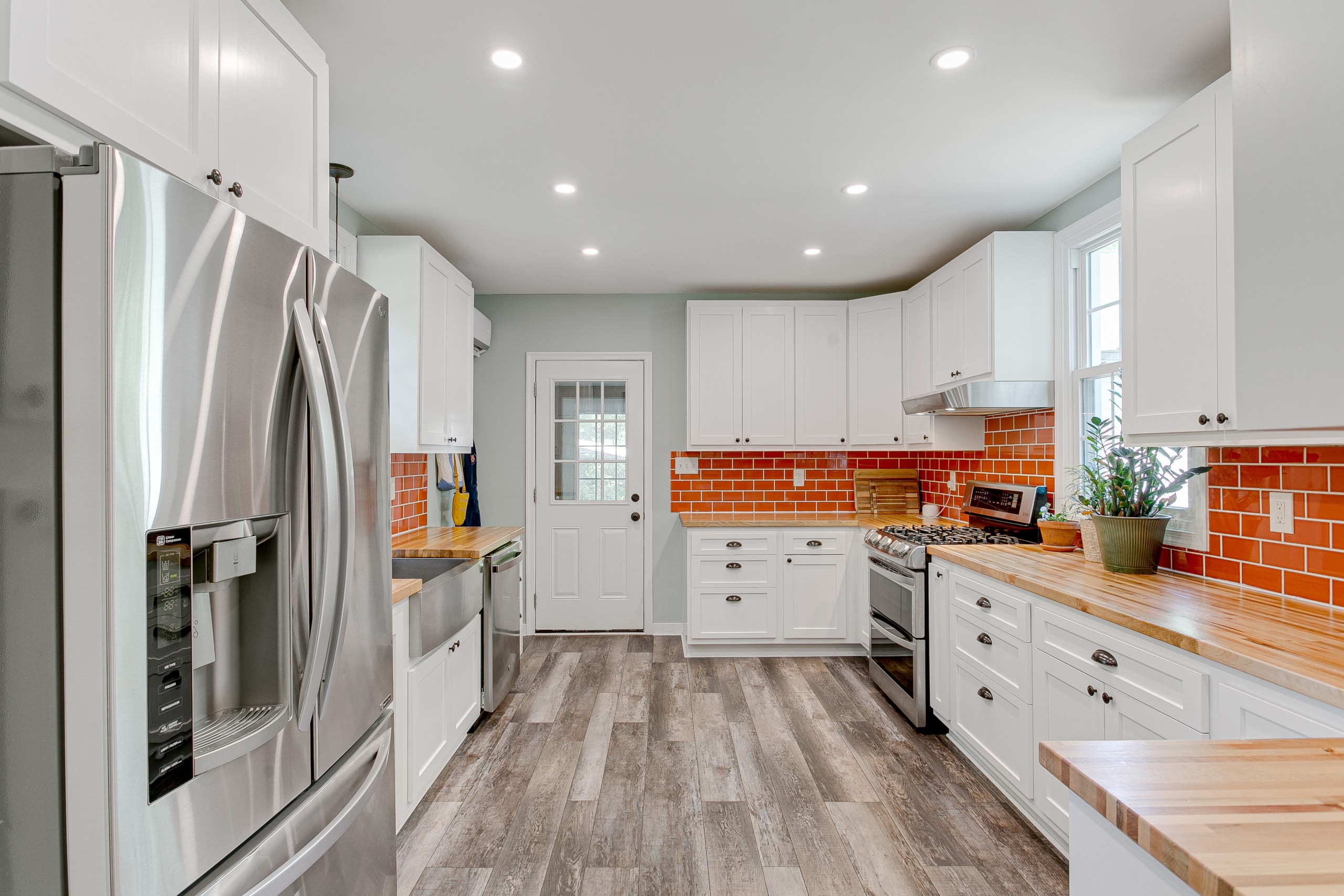 modern kitchen interior white cabinets black hardware bold orange red subway backsplash tile hardwood floors wooden butchers counter tops french doors plants recessed lighting fixture stainless steel